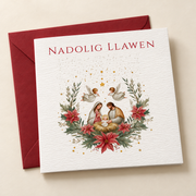 Cerdyn Nadolig Y Geni ac Angylion / Welsh Christmas card with a Nativity scene, angels and red flowers, lying flat beside a deep red envelope.