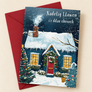 Cerdyn Nadolig i’r Ddau Ohonoch – Bwthyn / Welsh Christmas card with a blue cottage in the snow, lying flat beside a deep red envelope.