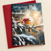 Cerdyn Nadolig Mab – Robin / Welsh Christmas card with a robin in a Christmas hat, lying flat beside a deep red envelope.