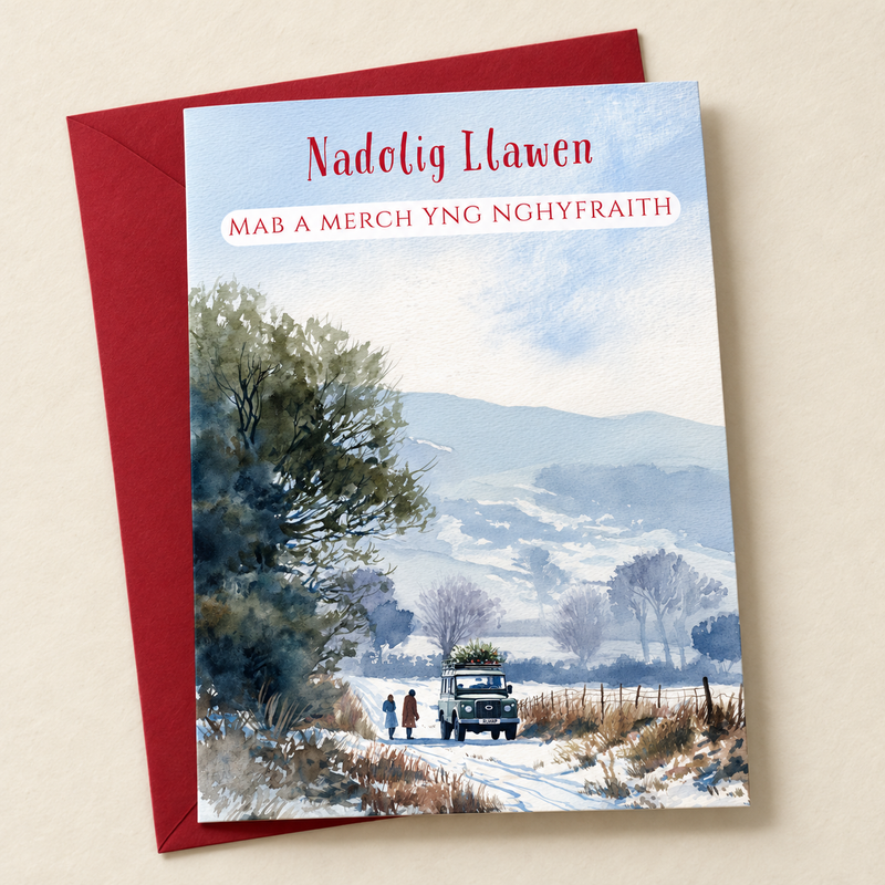 Cerdyn Nadolig Mab a Merch yng Nghyfraith – Eira / Welsh Christmas card with a winter countryside scene with a vehicle and two people, lying flat beside a deep red envelope.