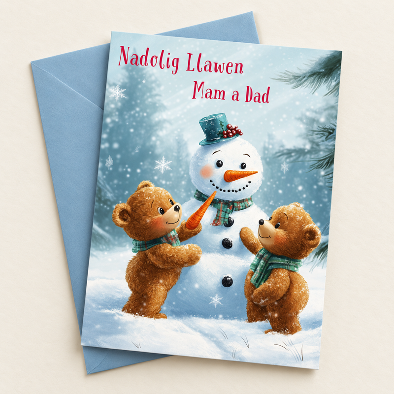 Cerdyn Nadolig Mam a Dad – Tedis a Dyn Eira / Welsh Christmas card with two teddies and a snowman, lying flat beside a soft blue envelope.