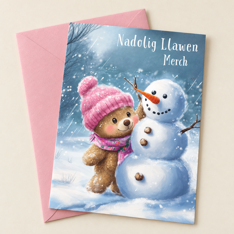 Cerdyn Nadolig Merch – Tedi / Welsh Christmas card with a teddy in a pink hat and a snowman, lying flat beside a soft pink envelope.