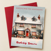 Cerdyn Nadolig Merch a Mab yng Nghyfraith – Bwthyn / Welsh Christmas card with a cottage with a red door in the snow, lying flat beside a deep red envelope.