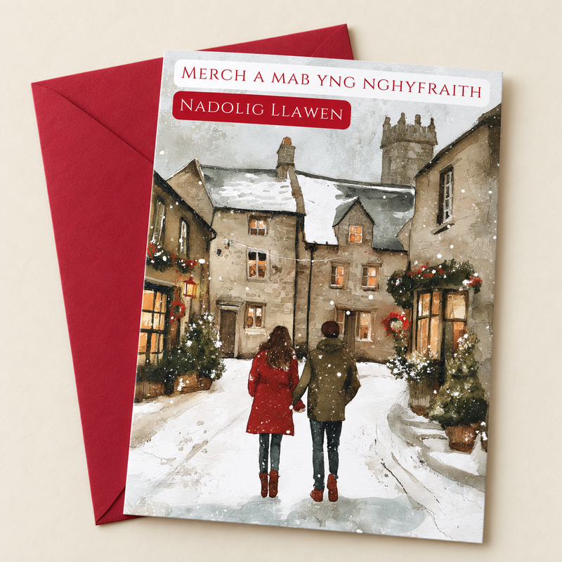 Cerdyn Nadolig Merch a Mab yng Nghyfraith – Pentref / Welsh Christmas card with two people walking through a snowy village, lying flat beside a deep red envelope.