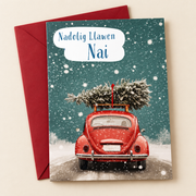Cerdyn Nadolig Nai – Car Coch / Welsh Christmas card with a red car carrying a Christmas tree, lying flat beside a deep red envelope.