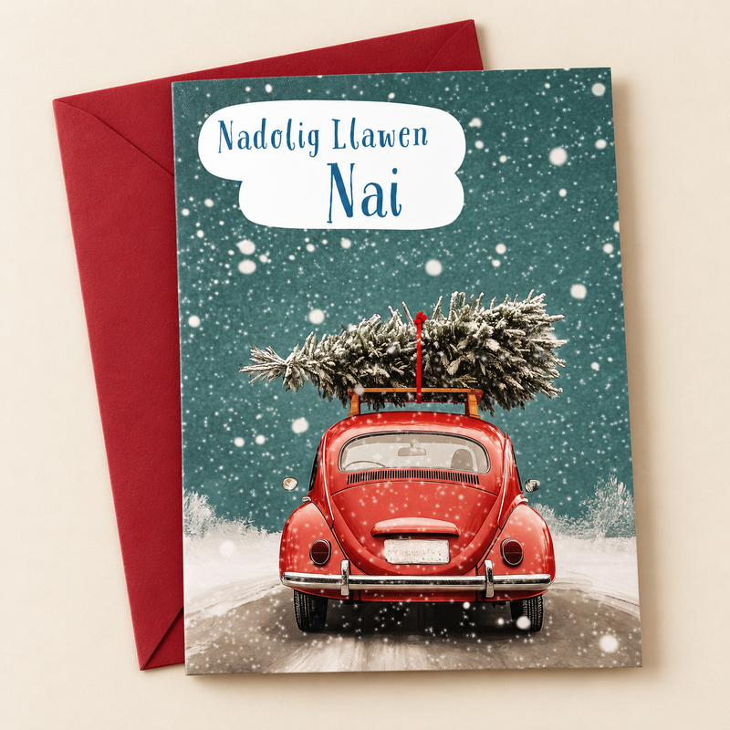 Cerdyn Nadolig Nai – Car Coch / Welsh Christmas card with a red car carrying a Christmas tree, lying flat beside a deep red envelope.