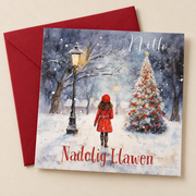 Cerdyn Nadolig Nith – Coeden Nadolig / Welsh Christmas card with a girl in a red coat beside a Christmas tree, lying flat beside a deep red envelope.