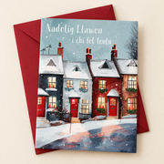 Cerdyn Nadolig i Chi fel Teulu – Tai / Welsh Christmas card with a row of houses in the snow, lying flat beside a deep red envelope.