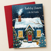 Cerdyn Nadolig i Chi fel Teulu – Bwthyn / Welsh Christmas card with a blue cottage in the snow, lying flat beside a deep red envelope.