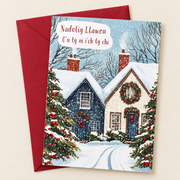 Cerdyn Nadolig O’n Tŷ Ni i’ch Tŷ Chi – Bythynnod / Welsh Christmas card with cottages and Christmas trees in the snow, lying flat beside a deep red envelope.