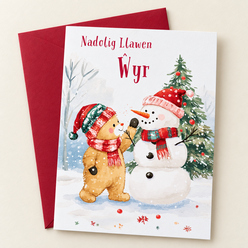 Cerdyn Nadolig Ŵyr – Tedi a Dyn Eira / Welsh Christmas card with a teddy and a snowman, lying flat beside a deep red envelope.