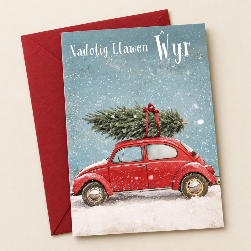 Cerdyn Nadolig Ŵyr – Car Coch / Welsh Christmas card with a red car carrying a Christmas tree, lying flat beside a deep red envelope.