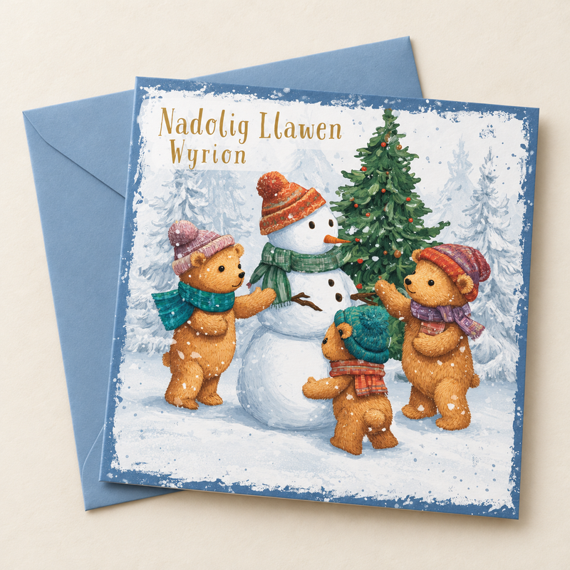 Cerdyn Nadolig Wyrion – Tedi Bêrs / Welsh Christmas card with teddy bears and a snowman beside a Christmas tree, lying flat beside a soft blue envelope.