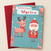 Cerdyn Nadolig Wyrion – Siôn Corn / Welsh Christmas card with Father Christmas and a reindeer on a teal background, lying flat beside a deep red envelope.