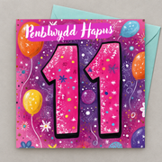 Cerdyn pen-blwydd 11 oed gyda rhif 11 pinc, blodau a balwnau, yn gorwedd yn fflat gydag amlen laswyrdd